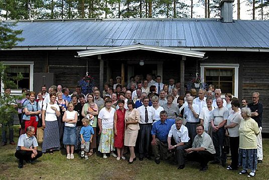 Ryhmä ihmisiä hirsirakennuksen edessä